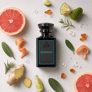 A bottle of Extrait de Parfum named 'MONACO' by the brand 'EMIHR ESSENCE, styled in a flat-lay with citrus fruits, herbs, and spices on a light gray background.